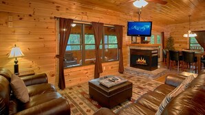Ein gemütliches Blockhaus-Interieur mit Ledersofas, einem Kamin, einem Fernseher und einem Essbereich.