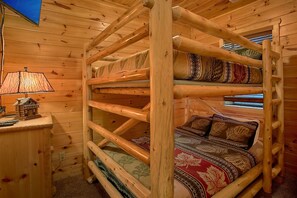 Cama litera de varios niveles con estructura de madera, una lámpara en una mesita de noche y una ventana con persianas.