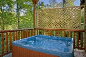Un jacuzzi en una terraza de madera con fondo de celosía, rodeado de árboles.