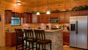 Eine Küche mit Holzausstattung, einer Steineninsel und einem Edelstahlkühlschrank.