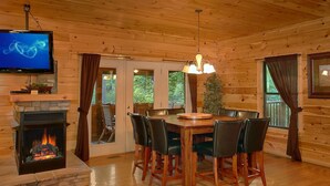 Ein Holzblockhaus-Interieur mit Kamin, Esstisch, Stühlen und einem Fernseher.