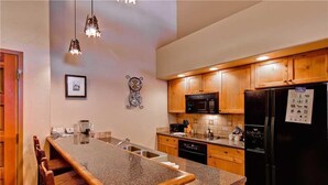 A kitchen with wooden cabinets, a black refrigerator, a microwave, and a granite countertop. - Tl2310 Spacious top Floor Residence! Winter Specials! (Steamboat Springs)