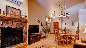 A living room with a stone fireplace, a television, a dining table with chairs, and a chandelier. - Tl2310 Spacious top Floor Residence! Winter Specials! (Steamboat Springs)