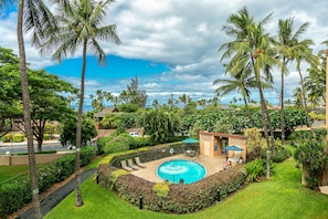 A swimming pool surrounded by palm trees and a small building with a patio. - Oceanview Condo | Walk to Beach | A/C | Pool | Tennis | Modern Comfort (Kihei)