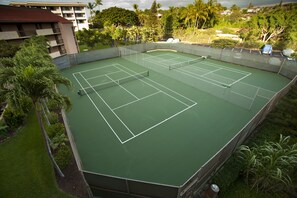 A tennis court surrounded by greenery and a building. - Oceanview Condo | Walk to Beach | A/C | Pool | Tennis | Modern Comfort (Kihei)