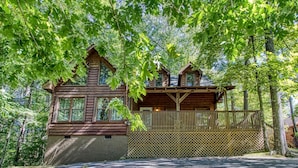 A log cabin with a balcony, surrounded by dense forest. - Whispering Oaks - Private Pigeon Forge Getaway...Close to Tanger Outlet Shopping (Sevierville)