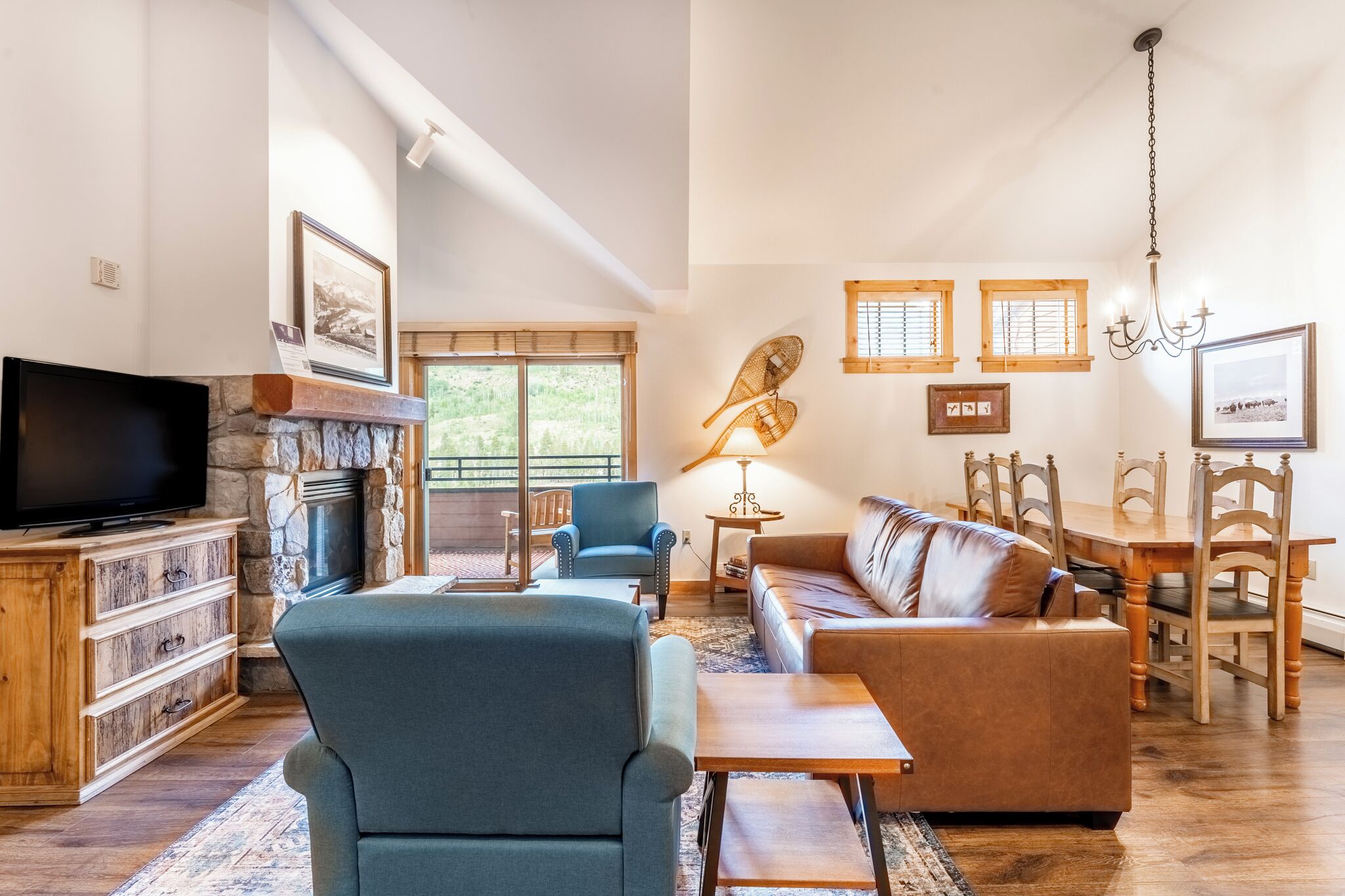 A spacious living room with a stone fireplace, comfortable seating, a television, and a dining area with wooden furniture.