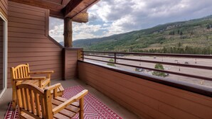 A wooden deck with two chairs and a patterned rug, overlooking a parking lot and green hills. - Ideal Location in River Run, Beautiful Mountain Views, Close to Gondola/Shops (Keystone)