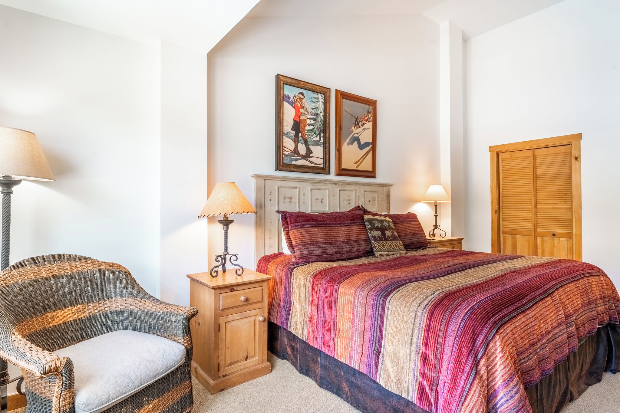 Une chambre à coucher avec un lit, deux lampes, une chaise, une armoire en bois et deux tableaux encadrés accrochés au mur.