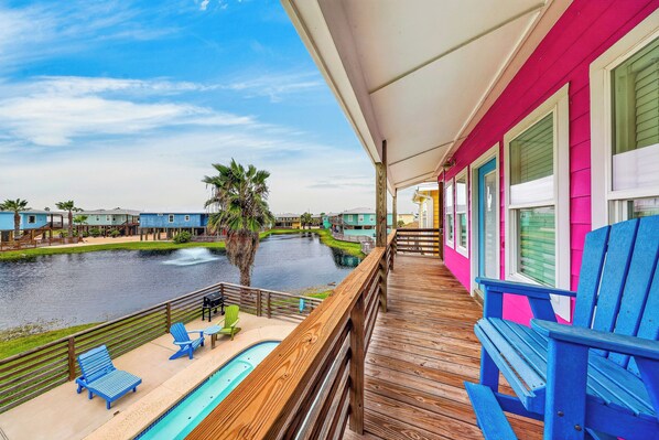 A wooden deck with a pool, chairs, and a view of a water body and buildings.