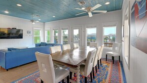 A dining area with a wooden table, white chairs, a blue sofa, and a ceiling fan. - Come stay and play at the Cherry on Top, Ocean Village’s premier rental! Private (Port Aransas)