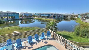 A pool area with blue Adirondack chairs and a small pool, surrounded by a wooden deck and a clear view of a calm lake. - Come stay and play at the Cherry on Top, Ocean Village’s premier rental! Private (Port Aransas)