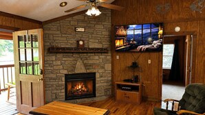 Ein gemütliches Zimmer mit Kamin aus Stein, Deckenventilator aus Holz und einem an der Wand befestigten Fernseher.
