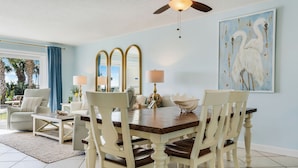 Un coin repas avec une table en bois, des chaises blanches et un grand tableau représentant un oiseau accroché au mur.