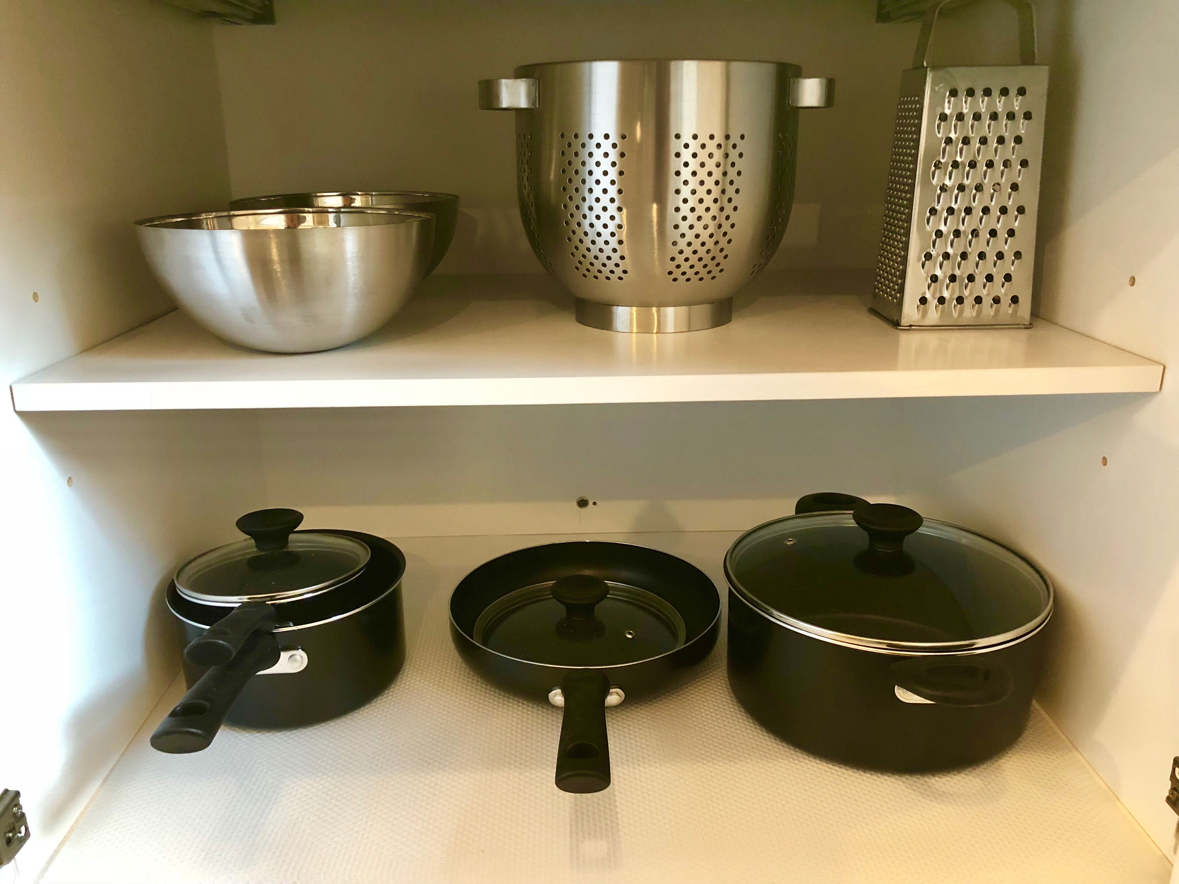Una repisa de cocina con utensilios de acero inoxidable, incluyendo un colador, un rallador y ollas.