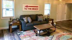 A cozy living room with a couch, a coffee table, and a sign pointing to the beach. - Renovated Cozy Chic North Fork Cottage, steps away from the Beach & Wine Trail!! (Calverton)