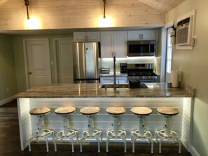 Una cocina moderna con electrodomésticos de acero inoxidable, encimera de granito y taburetes de bar con fustes de madera.
