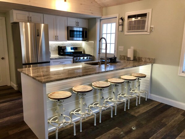 A modern kitchen with stainless steel appliances, a central island with bar stools, and a window with blinds.