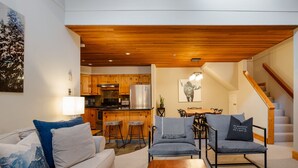 Una sala de estar moderna con techo de madera, una cocina con armarios de madera, un comedor y una escalera.