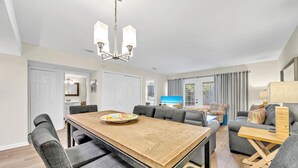 A spacious living area with a wooden dining table, grey upholstered chairs, a grey sofa, and a TV. - Beach Service Included, Private Beach, Chateau La Mer 9B! (Destin)
