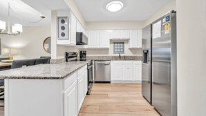 A modern kitchen with white cabinets, stainless steel appliances, and a granite countertop. - Beach Service Included, Private Beach, Chateau La Mer 9B! (Destin)