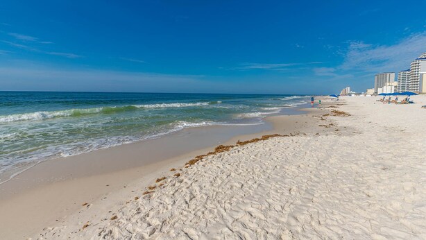 A beach with white sand, ocean waves, and buildings in the background.