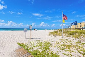 Une plage avec une promenade en bois, un mât portant le drapeau américain et un panneau d’affichage.