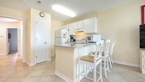 A kitchen with white cabinets, a built-in microwave, and a small island with chairs.
