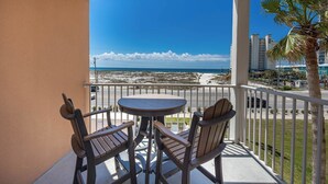A balcony with a round table and two chairs, overlooking a beach and cityscape.