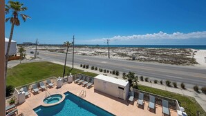 A pool area with lounge chairs and a view of the beach and ocean.