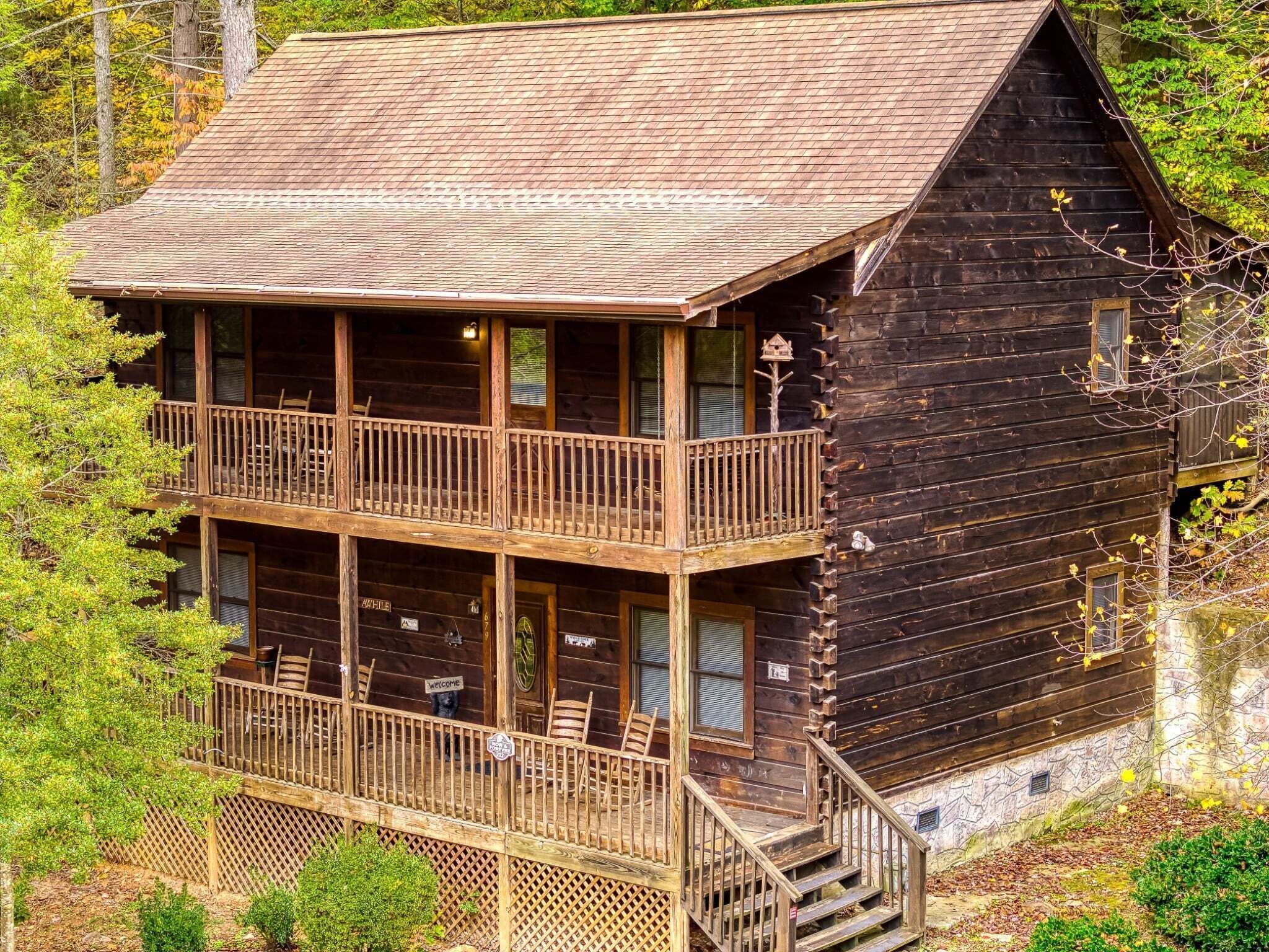 A two-story log cabin with a balcony and a staircase leading to the upper level.