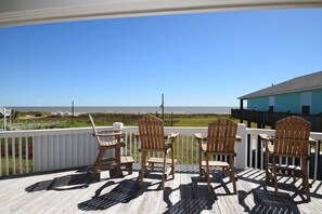 Terraza de madera con sillas Adirondack que dan a una playa.