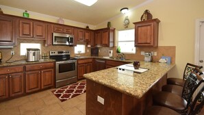 A kitchen with wooden cabinets, granite countertops, stainless steel appliances, and a central island. - Chateau Des Fontenot (Bolivar Peninsula)