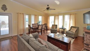 A living room with a sofa, a dining table with chairs, a ceiling fan, and a fireplace. - Chateau Des Fontenot (Bolivar Peninsula)