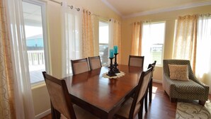 A dining room with a wooden table, chairs, a candle, and curtains. - Chateau Des Fontenot (Bolivar Peninsula)