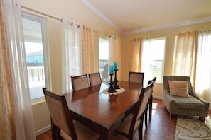 Un comedor con una mesa de madera, sillas, una vela y cortinas.