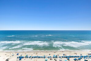 Ein Strand mit Reihen blauer Sonnenschirme und Liegen, ein sandiger Uferstreifen und der Ozean.