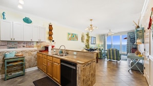 A kitchen with a built-in dishwasher, wooden cabinets, a granite countertop, and a view to the outside. - Beachy, Relaxing, Beachfront Condo, Great Location, Awesome Balcony Features (Panama City Beach)