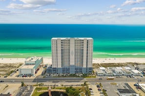 A high-rise hotel with multiple floors, a parking lot, and a beach view.