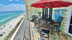 A balcony with a red umbrella, a table, and chairs overlooking a beach. - Beachy, Relaxing, Beachfront Condo, Great Location, Awesome Balcony Features (Panama City Beach)