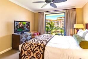 A hotel room with a bed, a television, a ceiling fan, and a view of a building through an open door.
