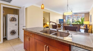 A kitchen with granite countertops, a built-in dishwasher, and a washing machine in the adjacent room.