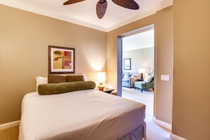 Une chambre d’hôtel avec un grand lit, un tableau au mur, une lampe et une vue sur une autre pièce où se trouvent un canapé et une table.