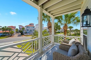 A covered porch with wicker furniture, a view of a street, and palm trees. - AQUASCAPE: Beautiful Home with Private Pool and Large Deck 1 Block from Beach! (Santa Rosa Beach)
