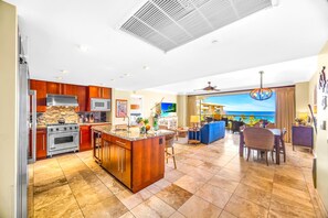 A spacious kitchen with a central island, a dining area with a view of the ocean, and a living room with a large window overlooking the sea.
