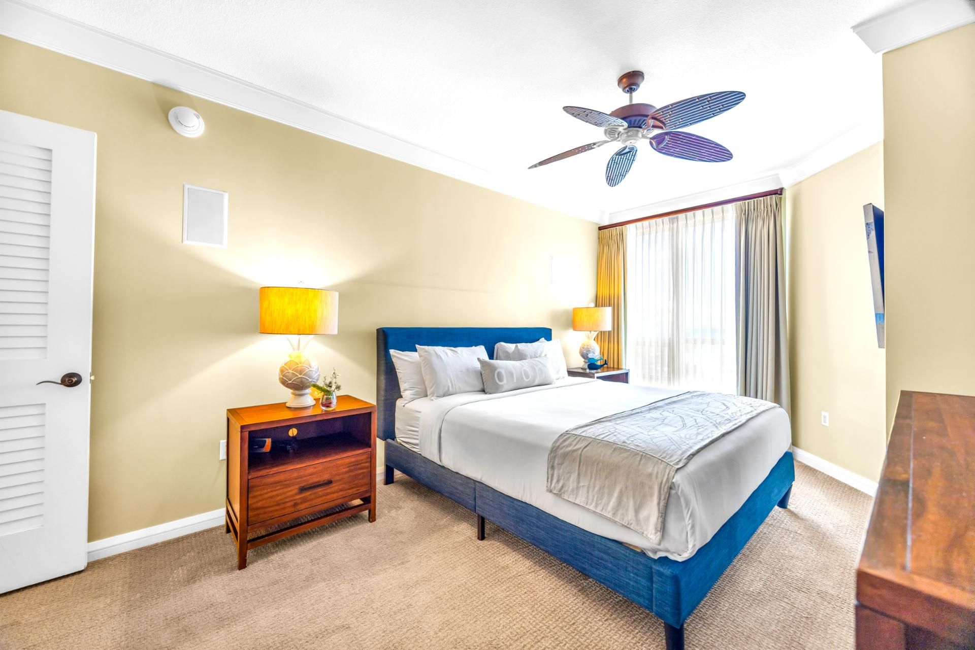 A hotel room with a bed, nightstands, a ceiling fan, and a window with curtains.