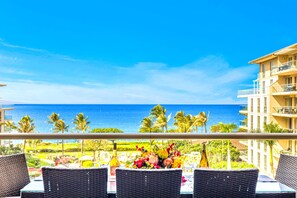 Varanda com cadeiras de vime e mesa posta para refeições, com vista para uma praia e oceano.