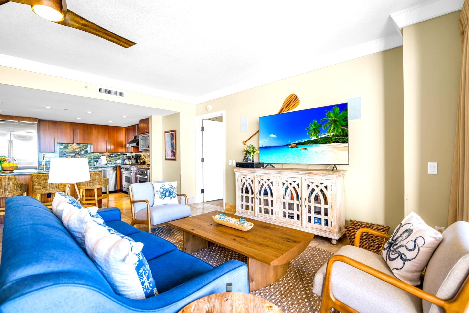 Ein modernes Wohnzimmer mit einem blauen Sofa, einem Holztisch und einem Fernseher, der eine tropische Strandlandschaft zeigt.