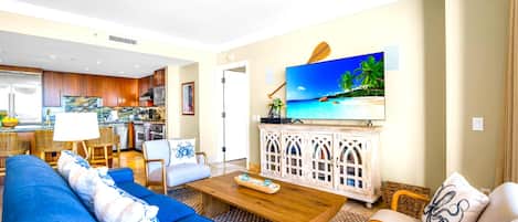 Ein modernes Wohnzimmer mit einem blauen Sofa, einem Holztisch und einem Fernseher, der eine tropische Strandlandschaft zeigt.