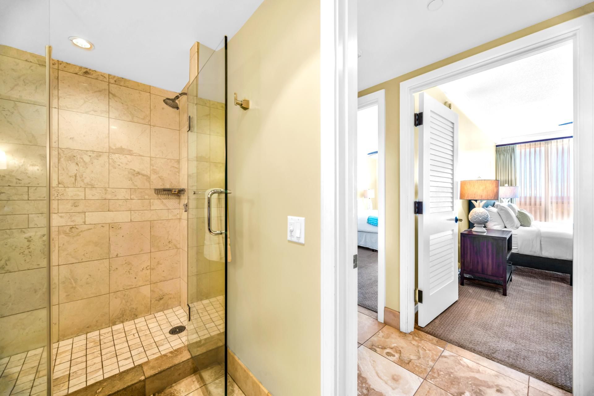 Une chambre d’hôtel avec une douche en verre, un lit avec une table de chevet et une vue sur le couloir.